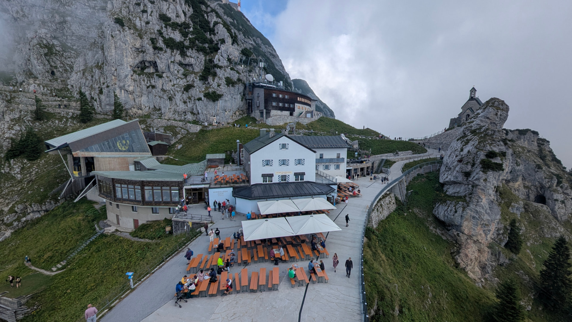 Wendelstein summit complex in the Bavarian Alps, with the Wendelstein-Haus restaurant terrace, cable car station, and the summit chapel perched on the rock spur.