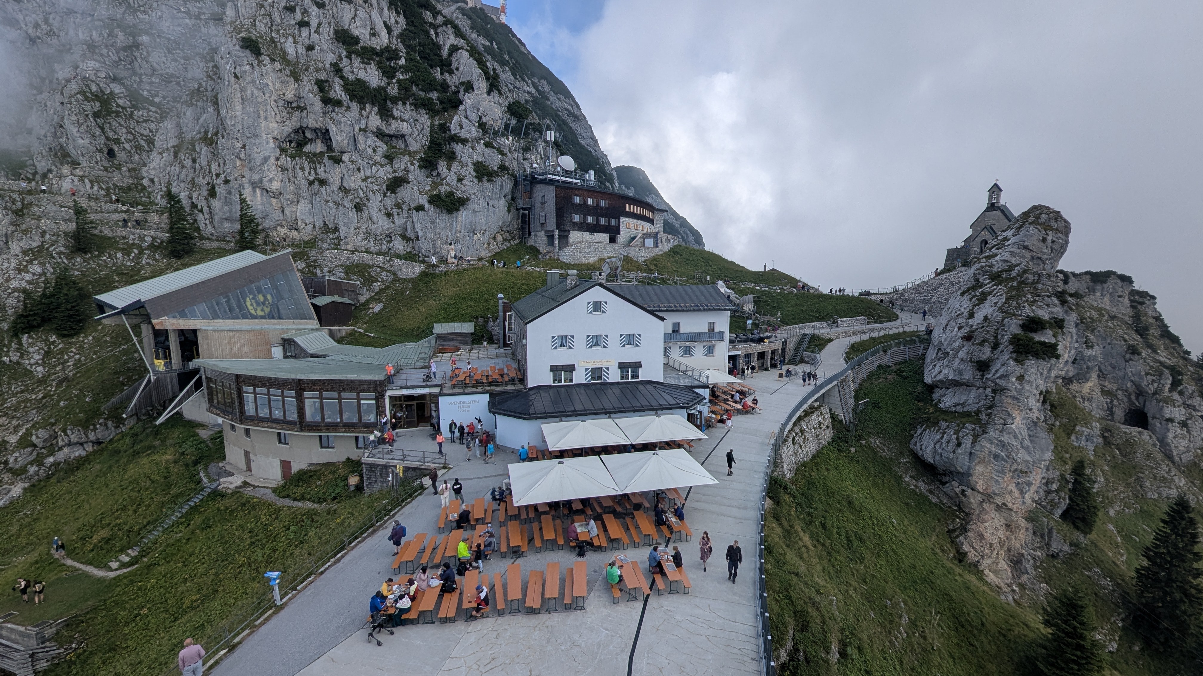 Wendelstein summit complex in the Bavarian Alps, with the Wendelstein-Haus restaurant terrace, cable car station, and the summit chapel perched on the rock spur.
