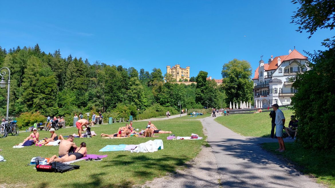 hohenschwangau-alpsee-summer-bavaria-germany people relaxing on grass by alpsee lake with view of hohenschwangau castle in summer, bavaria-germany